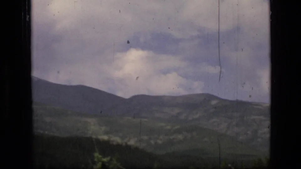 Scapegoat Wilderness landscape with layered ridges, forested lower slopes, cloudy sky, and visible 8mm wear.