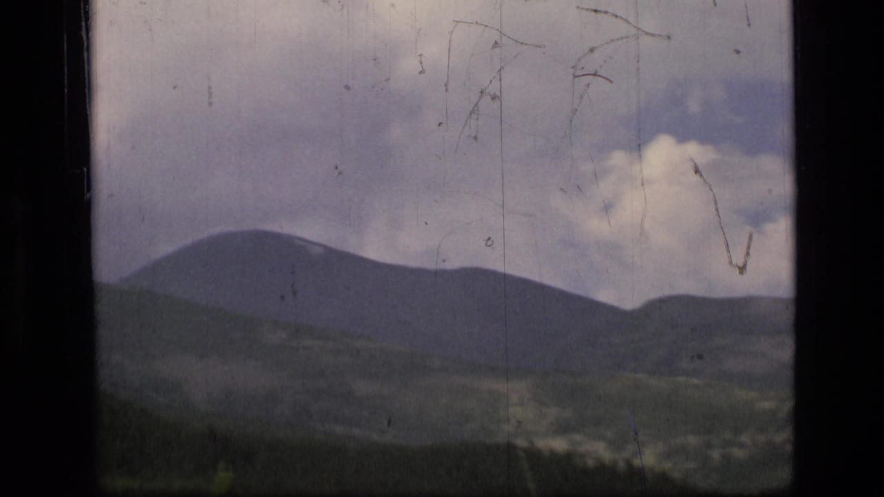 Mountain ridges beneath a cloudy sky, seen through scratched 8mm film.