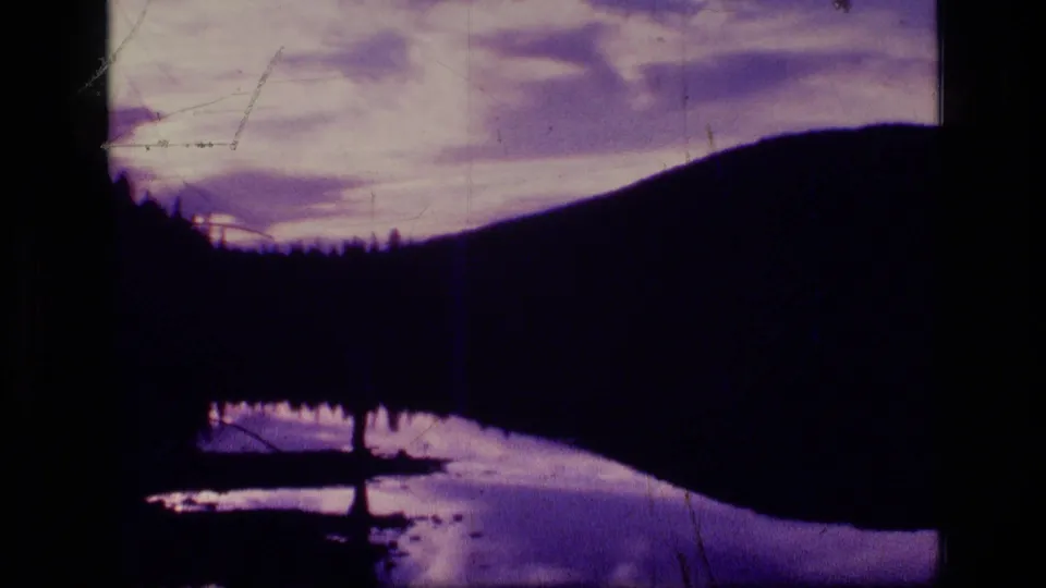 A silhouetted mountainside borders a calm lake at twilight in 1973 8mm footage from Scapegoat Wilderness, Montana.