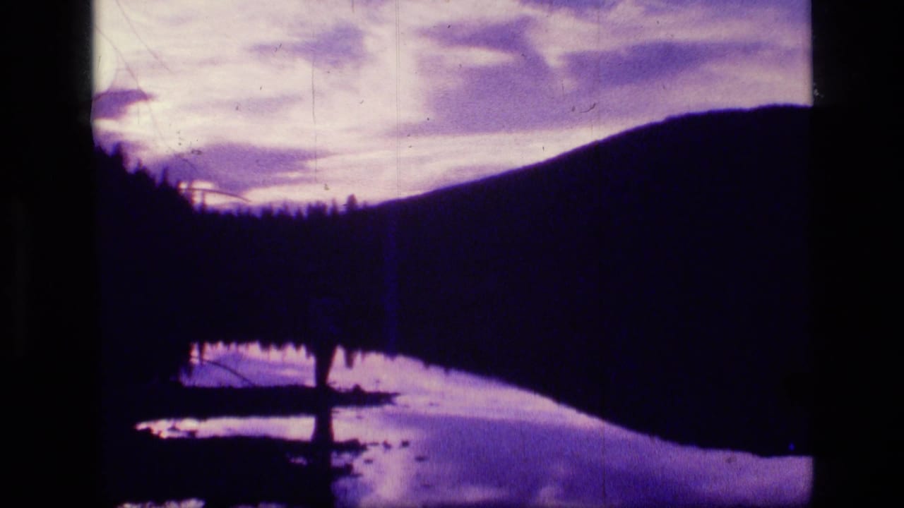 Purple dusk lake with dark hillside, tree line, and reflective water.