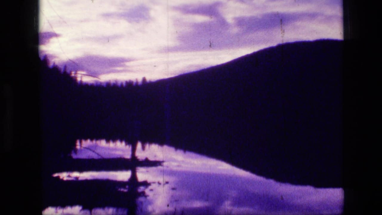 Scapegoat Wilderness lake scene with silhouetted hillside, shoreline trees, and purple-white cloud reflections on water.