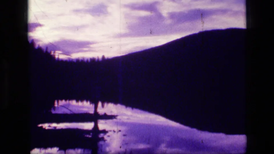 Scapegoat Wilderness lake scene with silhouetted hillside, shoreline trees, and purple-white cloud reflections on water.