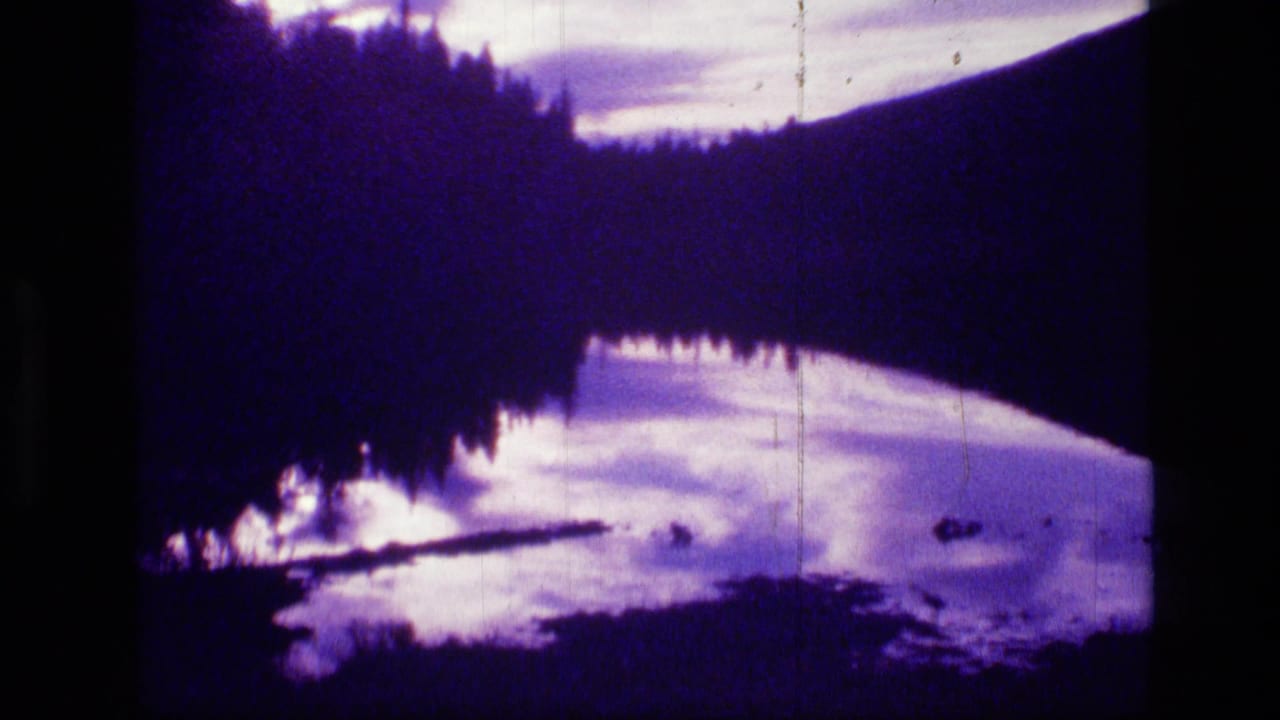 Scapegoat Wilderness landscape on 8mm film, showing a dark wooded slope, water reflection, pale clouds, and shoreline silhouettes.