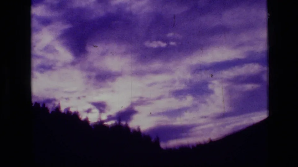 1973 8mm frame from Scapegoat Wilderness showing purple clouds over a silhouetted treeline.