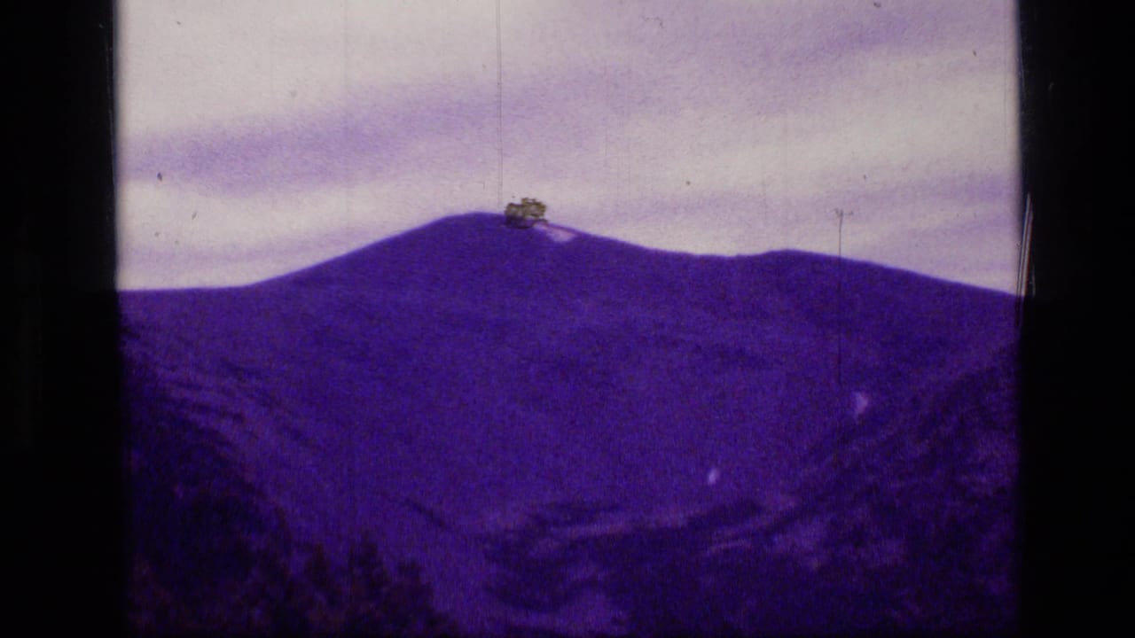 Scapegoat Wilderness mountain view on 1973 8mm film, showing a purple-tinted ridge, cloudy sky, and physical film artifacts.