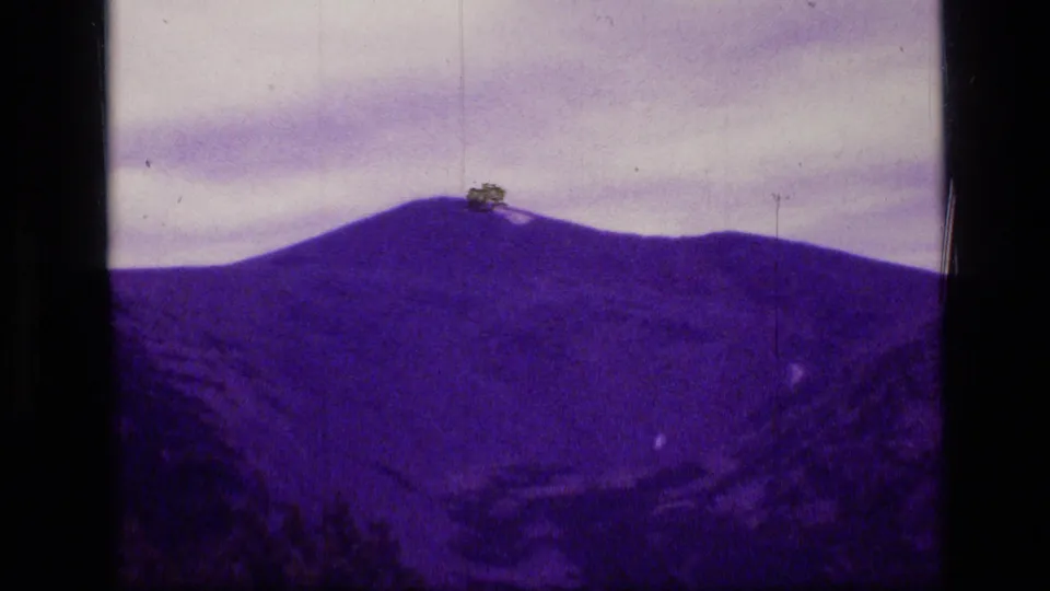 Scapegoat Wilderness mountain view on 1973 8mm film, showing a purple-tinted ridge, cloudy sky, and physical film artifacts.