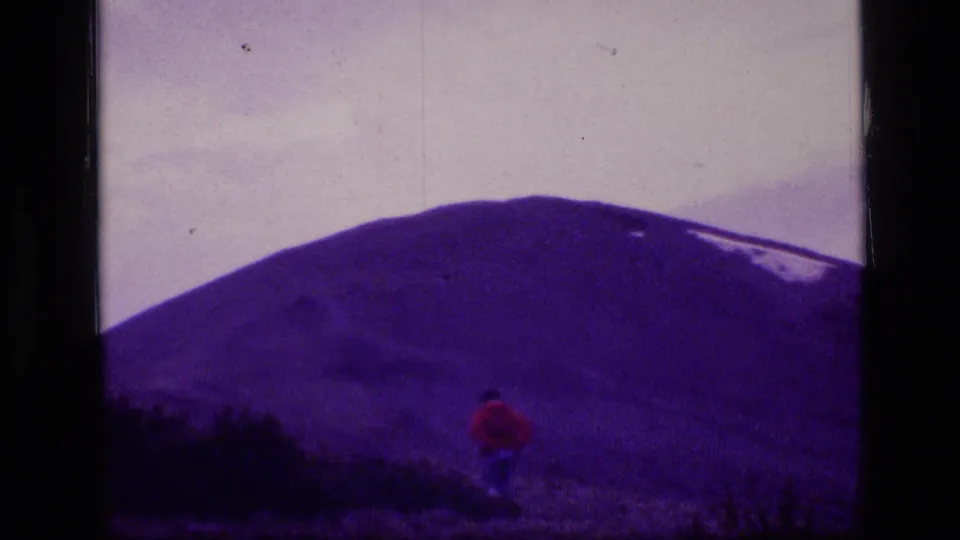 The final frame shows the red-jacketed hiker lower on the trail beneath the large purple-shifted mountain slope.