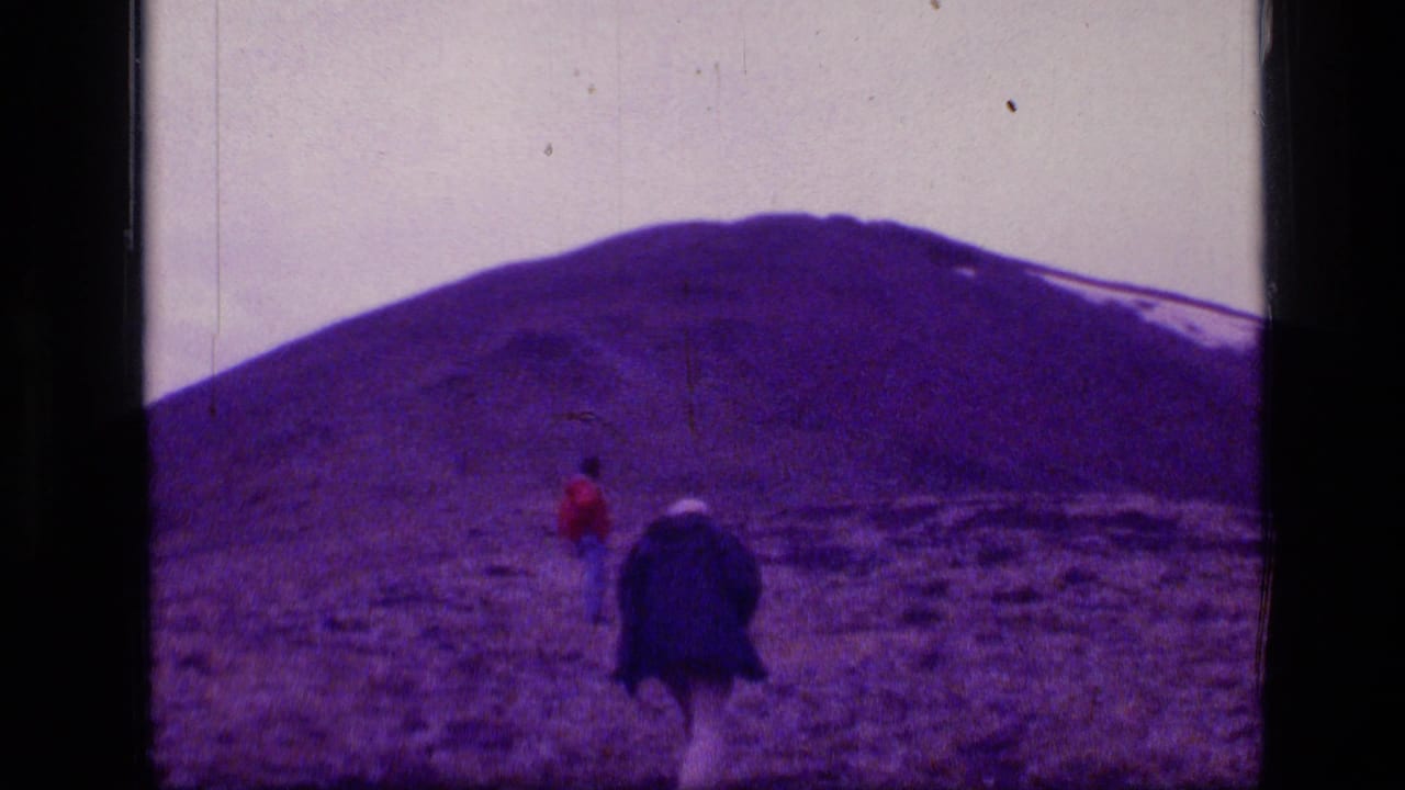 Two small figures in Scapegoat Wilderness, Montana, appear near a dark object or pack below a broad snow-streaked mountain slope.