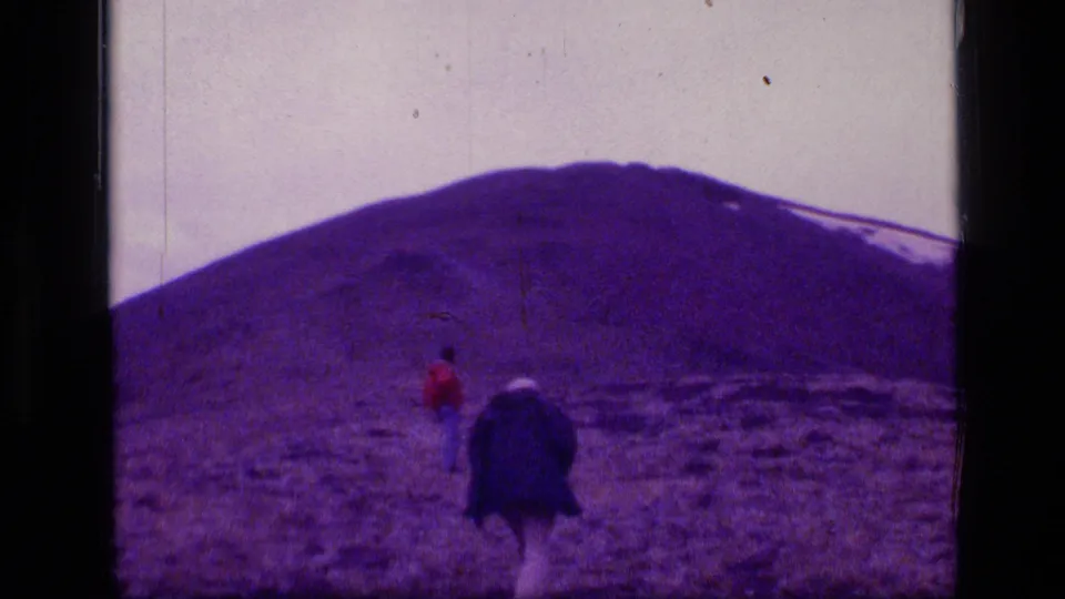Two small figures in Scapegoat Wilderness, Montana, appear near a dark object or pack below a broad snow-streaked mountain slope.