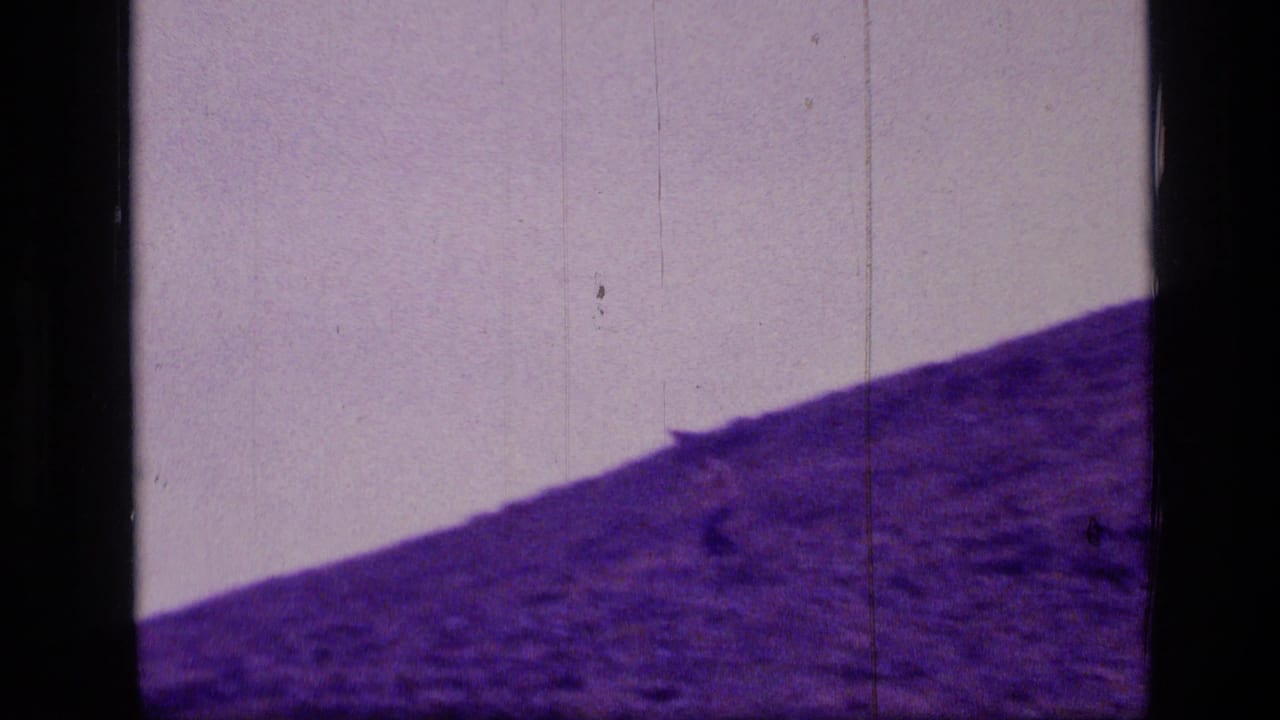 A distant person crosses the upper part of a rocky Montana wilderness slope in purple-faded 8mm footage from 1973.