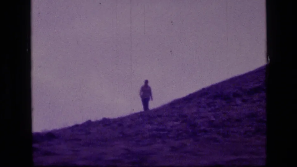 A distant figure in dark pants stands out on the purple-tinted rocky slope in 1973 Scapegoat Wilderness home-movie footage.