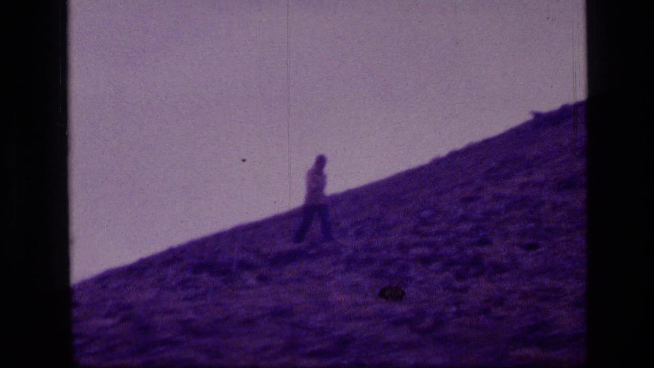 A lone walker moves along a slanted rocky slope in Scapegoat Wilderness, Montana, in purple-tinted 8mm home-movie footage.