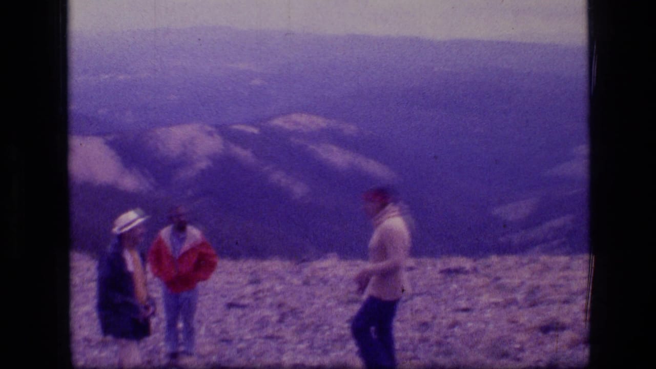 Three hikers stand on a rocky mountain summit with layered ridges behind them.