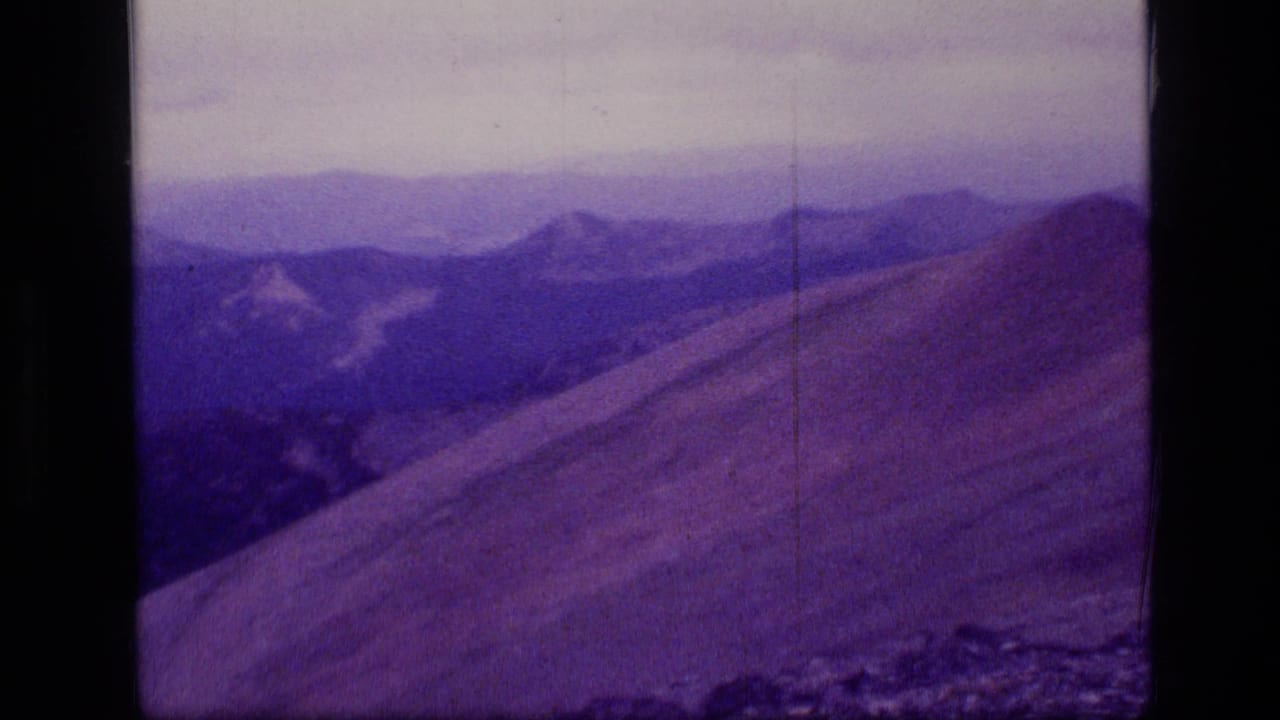 1973 Scapegoat Wilderness frame showing a sloped Montana ridgeline, distant peaks, haze, and visible 8mm film borders.