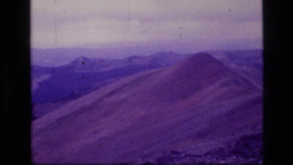 Purple-shifted 1973 8mm frame of Scapegoat Wilderness with a ridge crest, valley forms, and distant Montana mountains.
