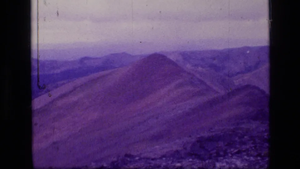 Final 1973 Montana wilderness frame showing a sloped ridge, rocky foreground, distant mountains, and aged 8mm texture.