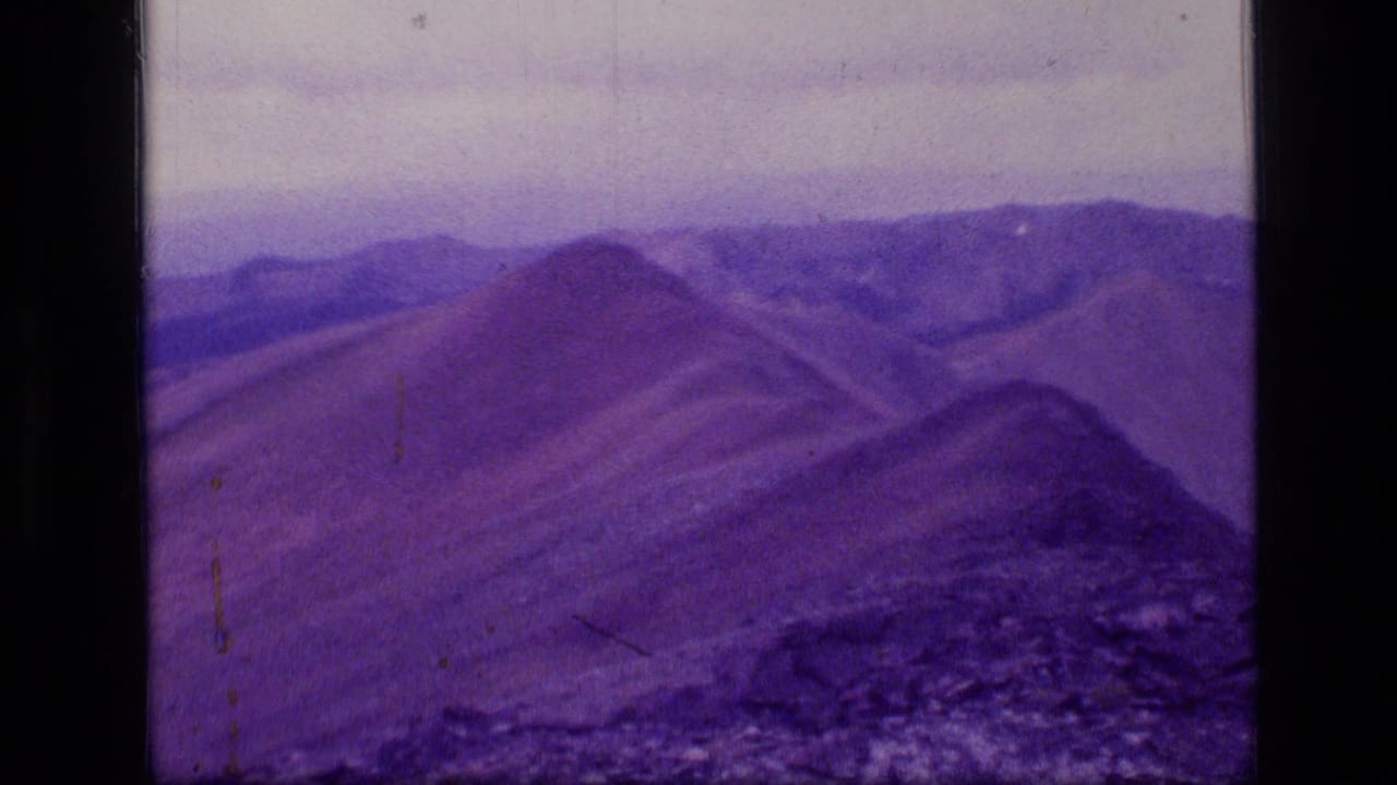 Purple-tinted mountain ridges under a hazy sky with rocky slope in foreground.