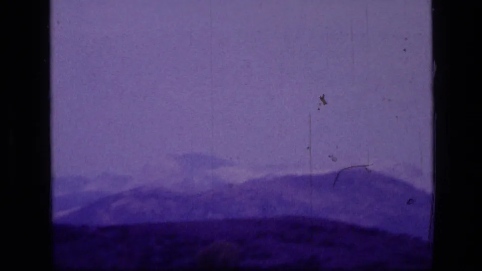 1973 8mm Montana landscape view with layered mountain ridges beneath a hazy purple-tinged sky.