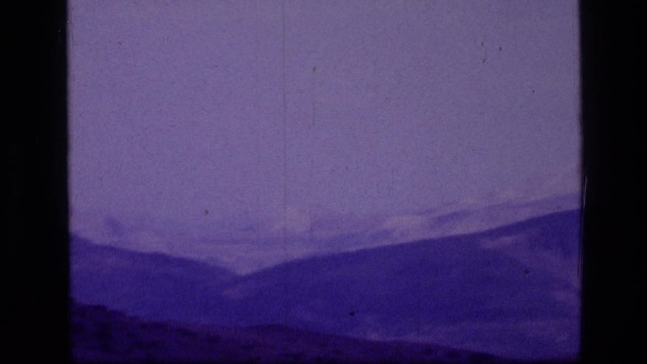 1973 Scapegoat Wilderness mountain ridges appear through purple-shifted 8mm film grain and dust marks.
