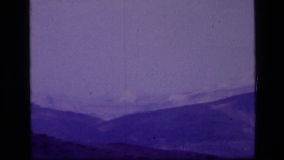 1973 Scapegoat Wilderness mountain ridges appear through purple-shifted 8mm film grain and dust marks.
