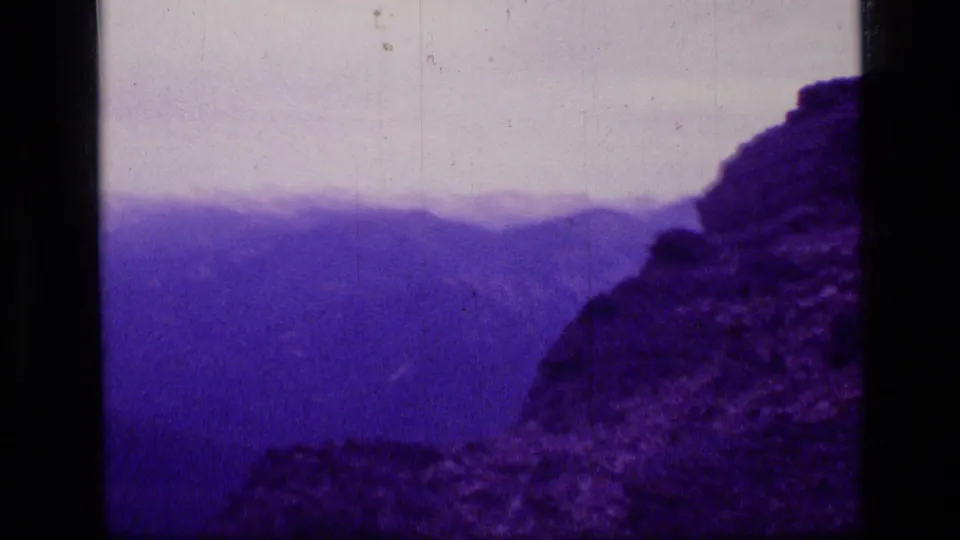 1973 Scapegoat Wilderness landscape frame showing a rocky slope in the foreground and layered purple mountain ridges in the distance.