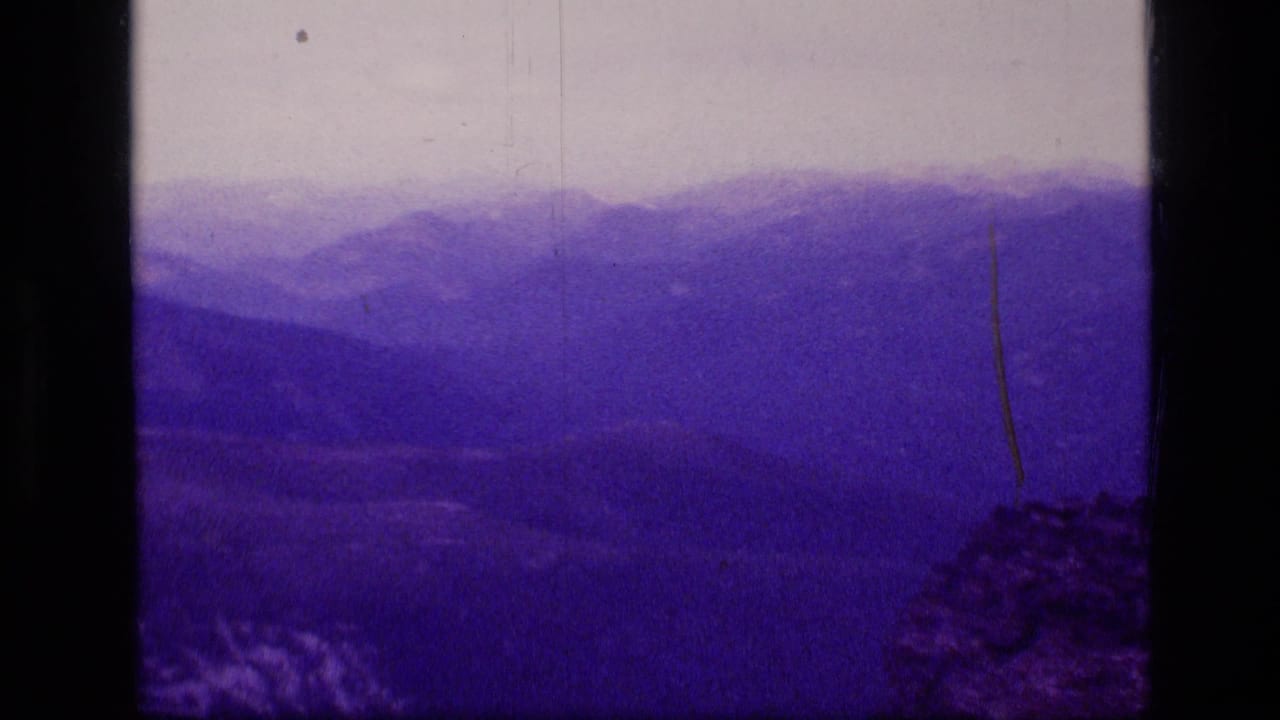 Faded 8mm frame of Montana wilderness ridges and a dim valley, with scratches and dark side borders visible.