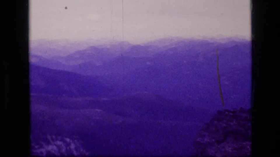Faded 8mm frame of Montana wilderness ridges and a dim valley, with scratches and dark side borders visible.
