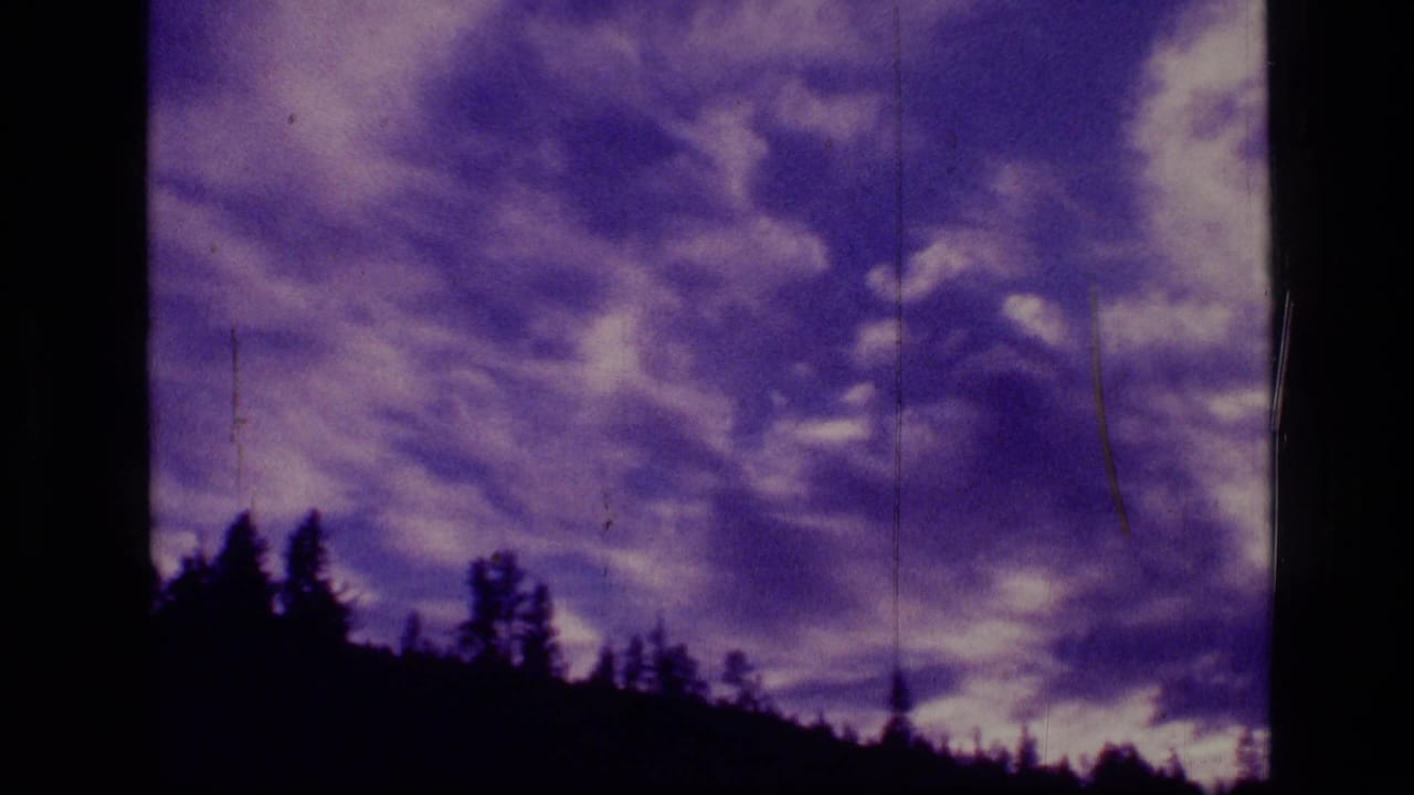 Purple-hued 8mm cloudscape over a dark evergreen ridge, supported by metadata as Scapegoat Wilderness, Montana in 1973.