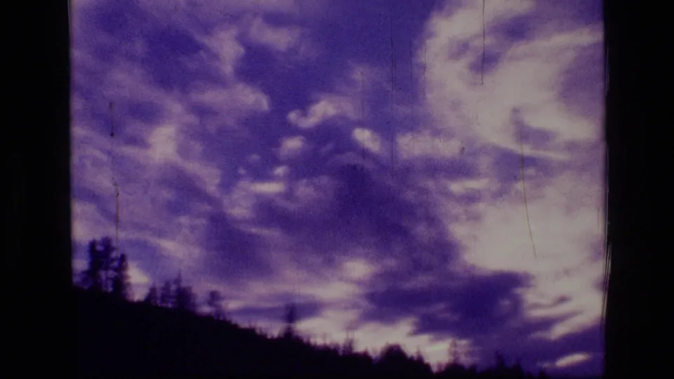 Vintage 8mm frame with bright cloud breaks and purple sky over a low evergreen silhouette in the Montana wilderness clip.