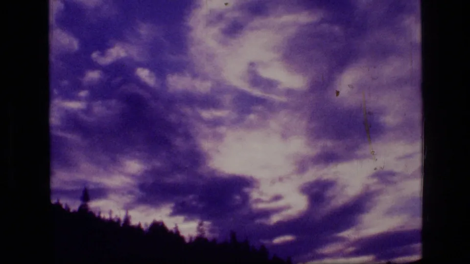 Final 8mm frame showing purple and white cloud masses over a dark wooded ridge in the supplied 1973 Scapegoat Wilderness footage.