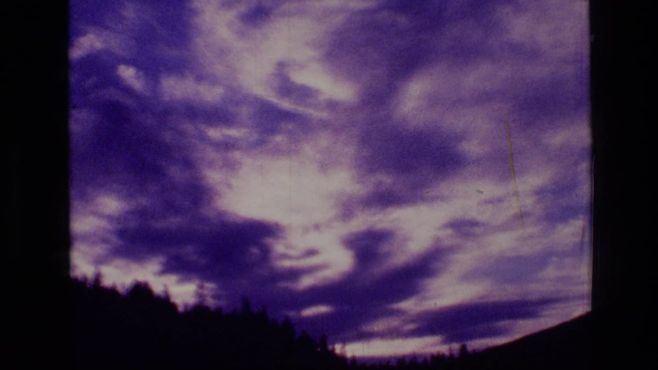 Violet sunset clouds above a dark forested ridge and mountain slope.
