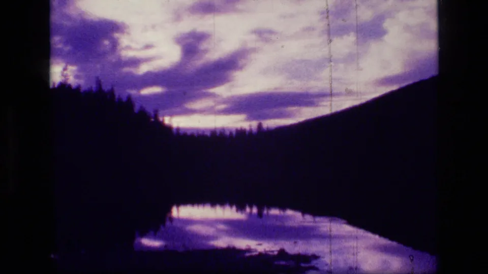 1973 Scapegoat Wilderness 8mm frame looking from violet sunset clouds down to a dark forest ridge and reflective lake.