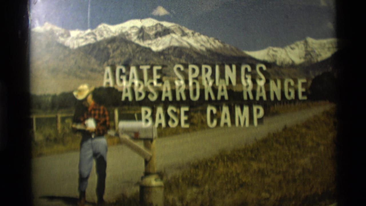 1975 Montana 8mm frame of a man in cowboy hat near a mailbox and Agate Springs base-camp sign, with the Absaroka Range behind.