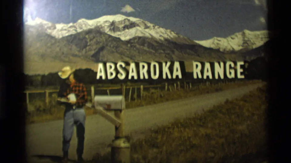 1975 Montana frame showing a cowboy-hatted man beside a mailbox, with readable Absaroka Range lettering over mountain scenery.