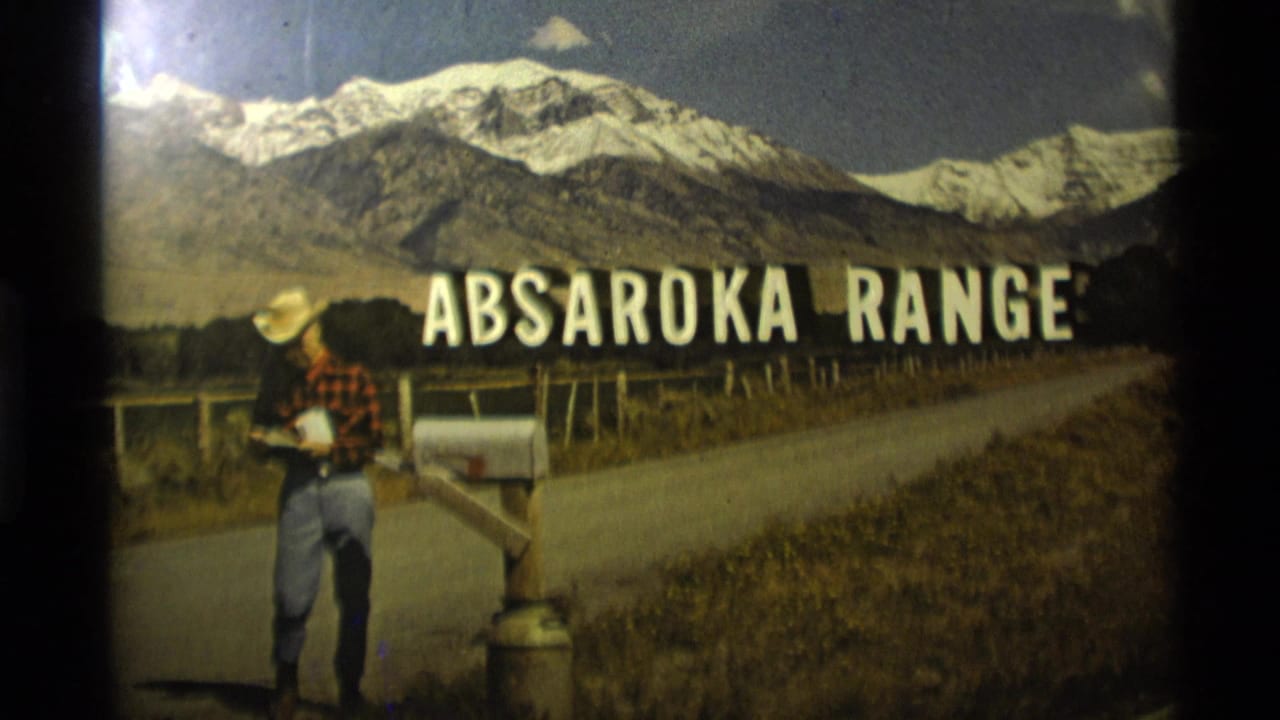 Man beside mailbox on rural road with Absaroka Range title and mountain backdrop.