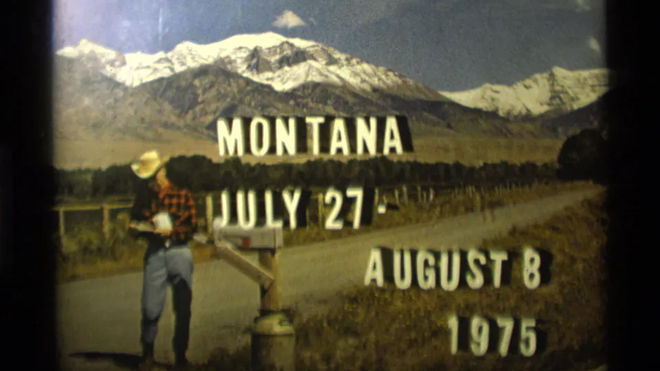 1975 Montana title card frame showing dates July 27-August 8 over a rural roadside mailbox scene with a man and mountain backdrop.