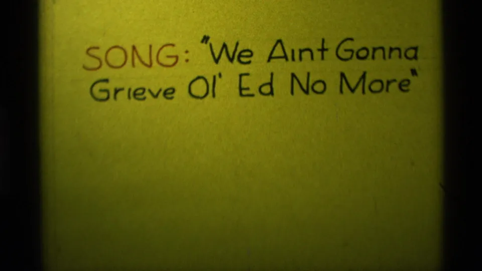 1975 8mm home-movie frame from Agate Springs, Montana showing the handwritten song title across a yellow card.