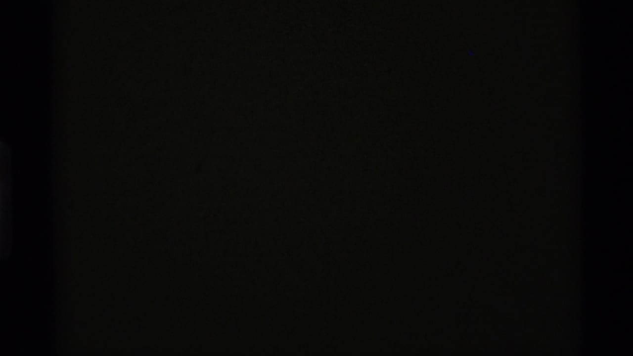 Dark opening frame from the 1975 8mm clip, with little visible detail beyond grain and faint edge density.