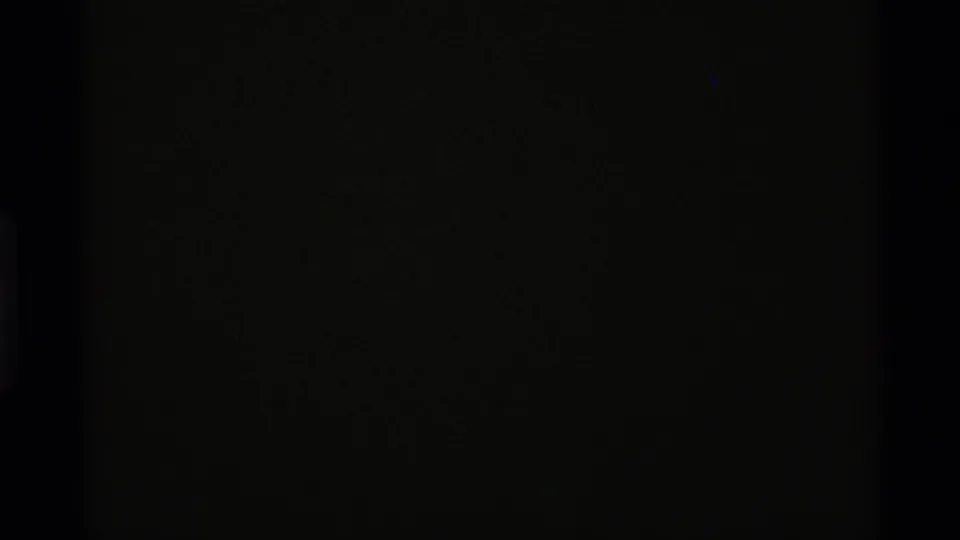 Dark opening frame from the 1975 8mm clip, with little visible detail beyond grain and faint edge density.