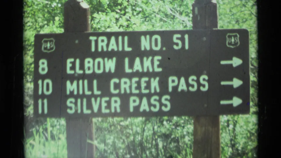 1975 Montana 8mm frame showing a forest trail sign for Trail No. 51 with mileage to Elbow Lake, Mill Creek Pass, and Silver Pass.