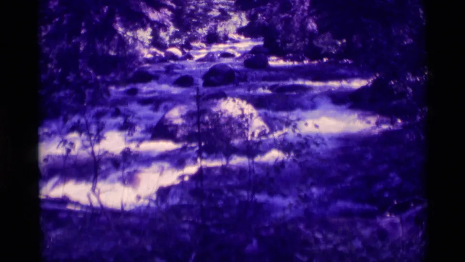 1975 Agate Springs, Montana home-movie frame showing white water moving through a rocky, tree-lined ravine.