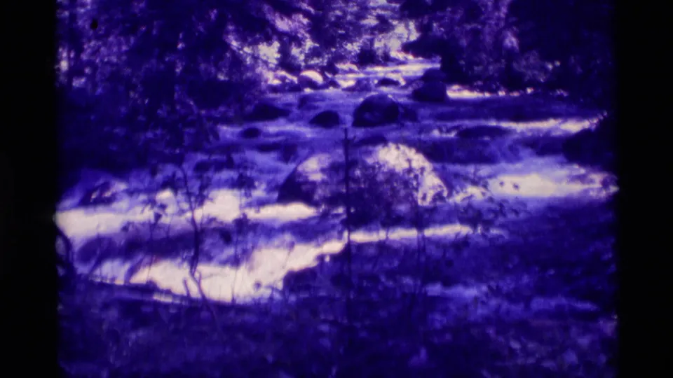 Vintage 8mm view of a rocky Agate Springs stream with bright rapids, boulders, and dark tree cover.