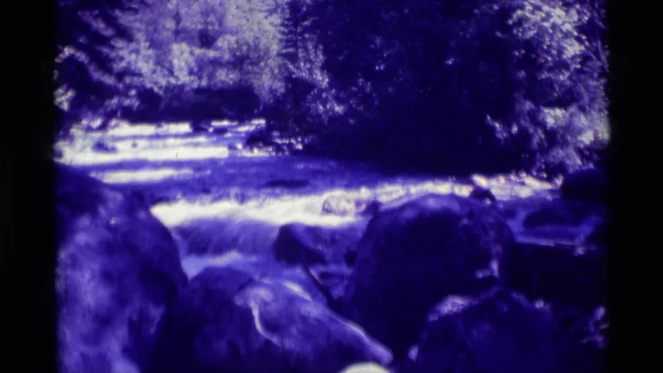 Agate Springs stream water appears to rush through shaded rocks and trees in blue-purple 8mm footage from 1975.