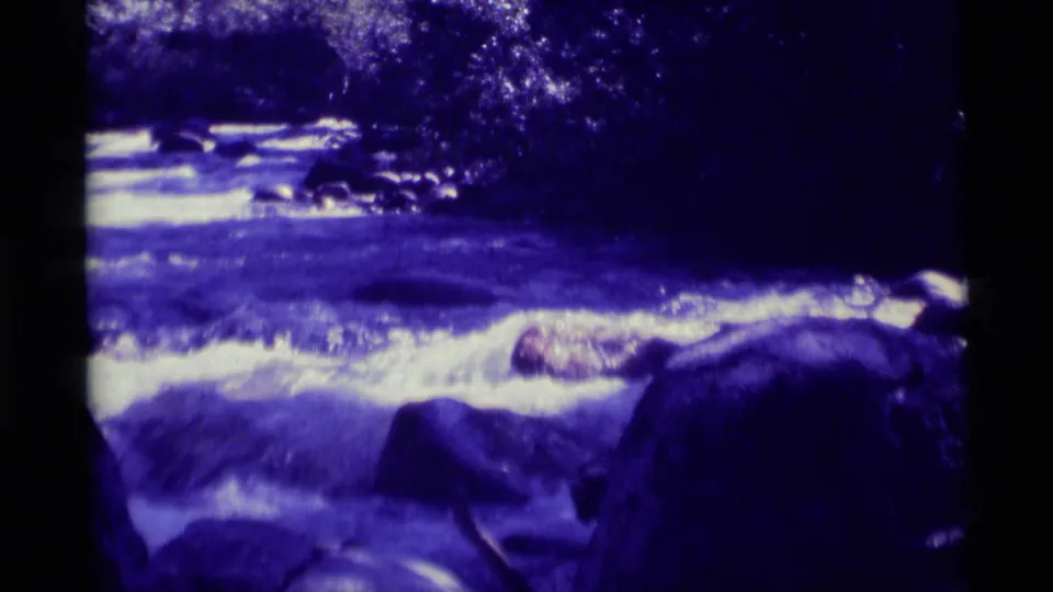 Final 1975 Agate Springs frame shows stream water crossing rocks with dark tree shadows and strong blue-purple archival color shift.