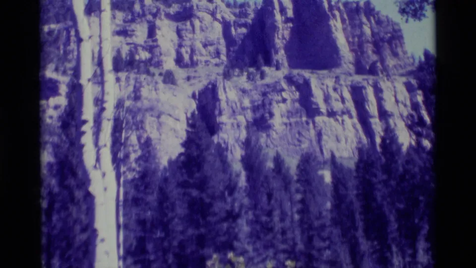 1975 8mm view of a rocky mountainside in Agate Springs, Montana, with evergreen trees below and visible film edge at left.
