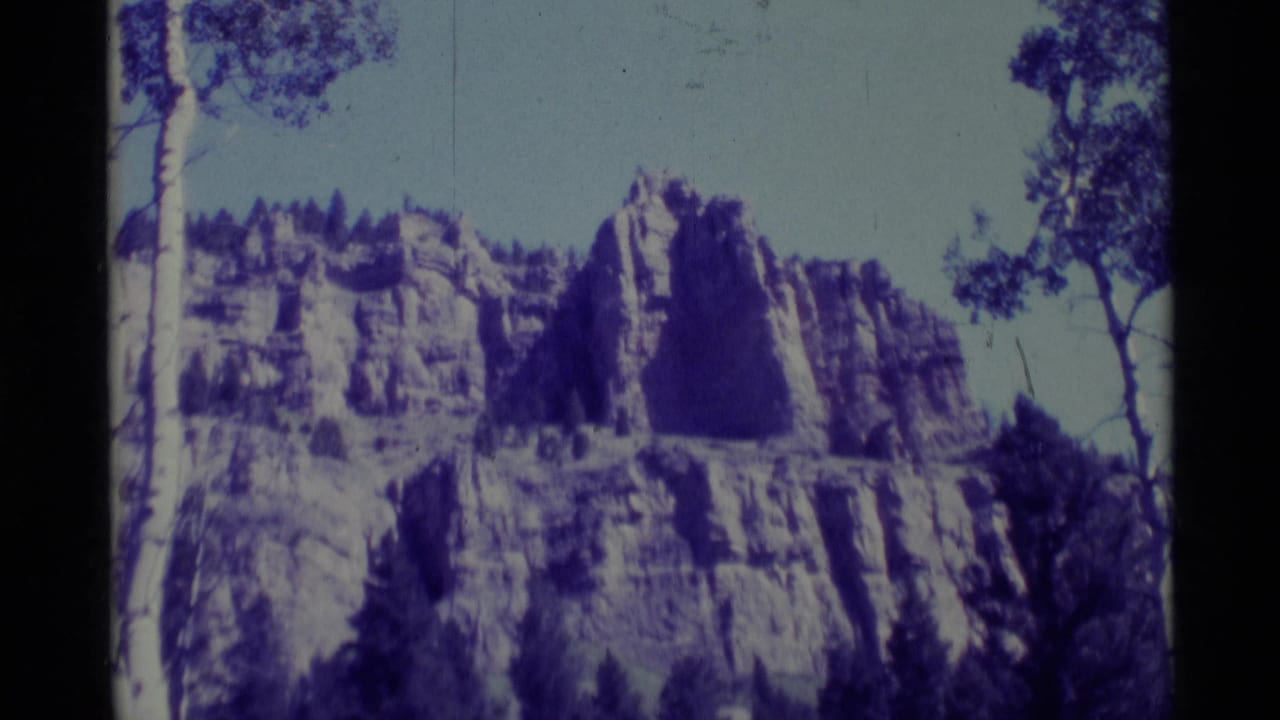 1975 Agate Springs, Montana 8mm view of a pale rock bluff rising above trees, tinted by a strong purple-blue color cast.