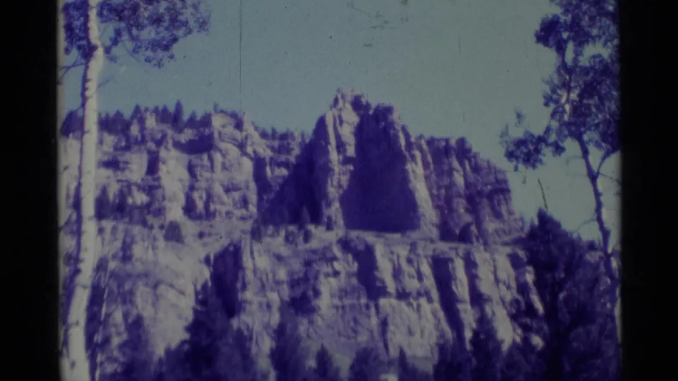 1975 Agate Springs, Montana 8mm view of a pale rock bluff rising above trees, tinted by a strong purple-blue color cast.