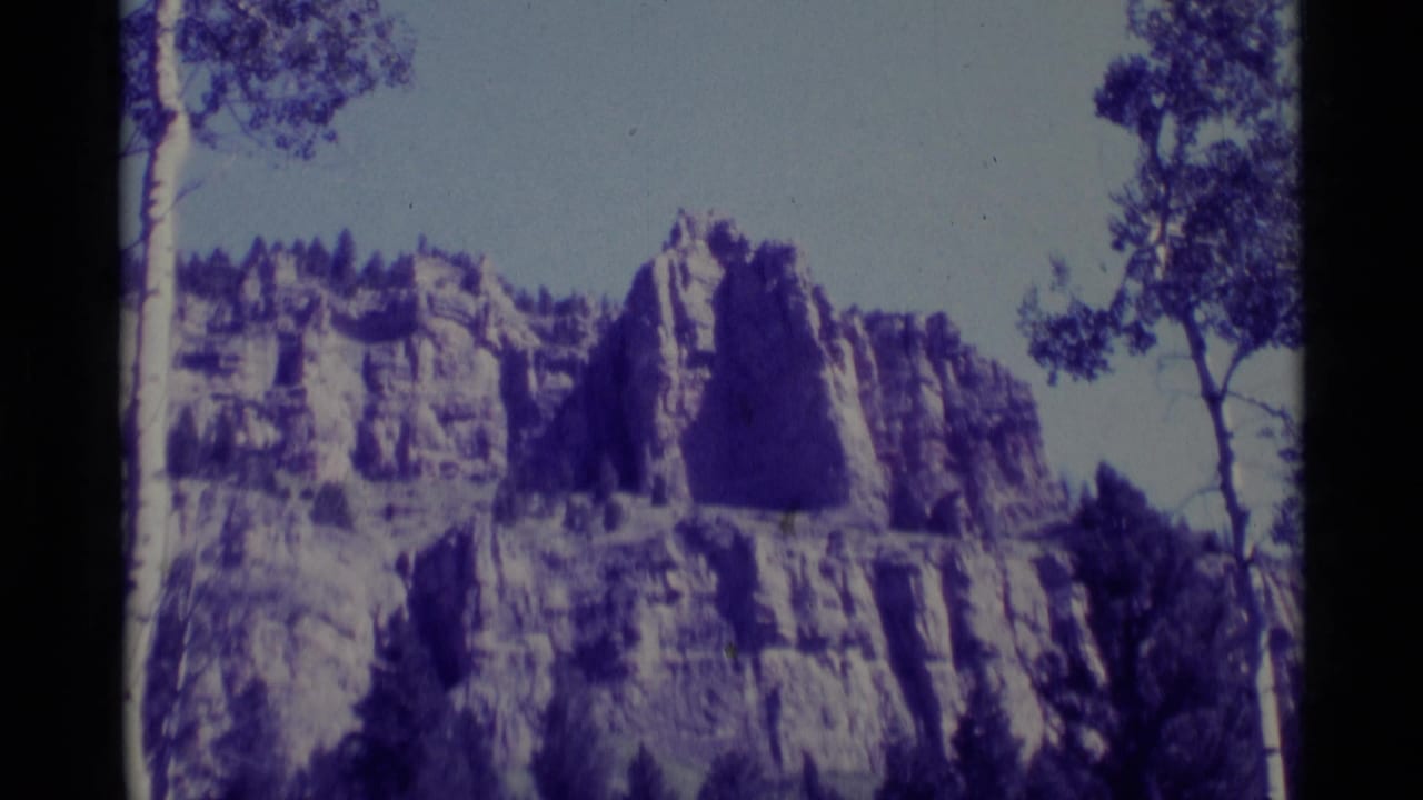 Rocky cliff face framed by trees, with pale sky and dark film borders.