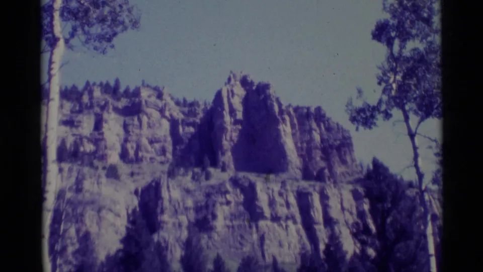 1975 Agate Springs, Montana 8mm frame showing a rugged cliff face framed by trees under a pale sky.