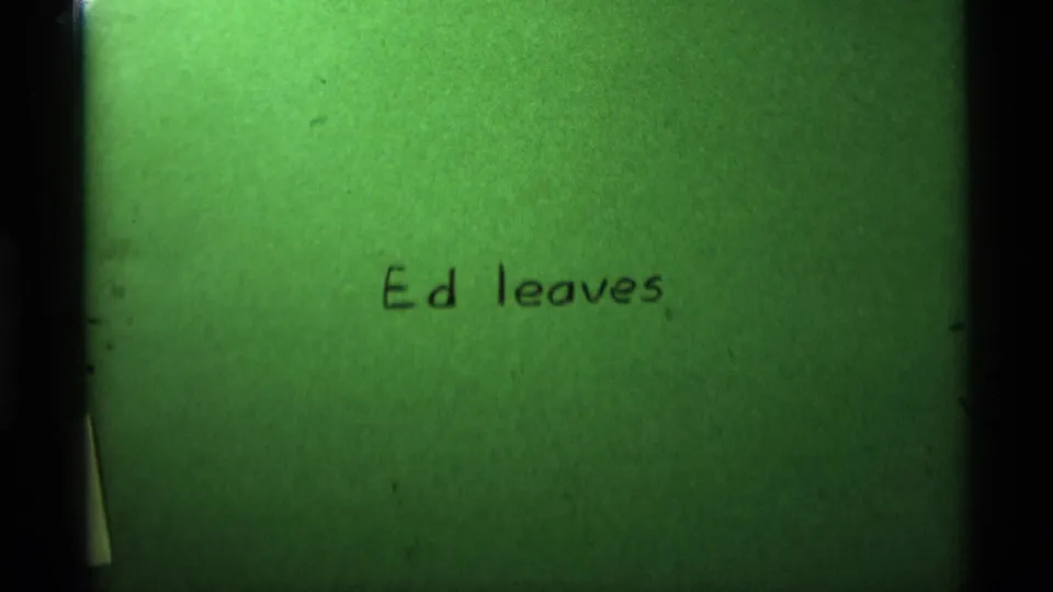 Green-tinted 8mm title card reading Ed leaves, with soft focus and dark film-frame edges.